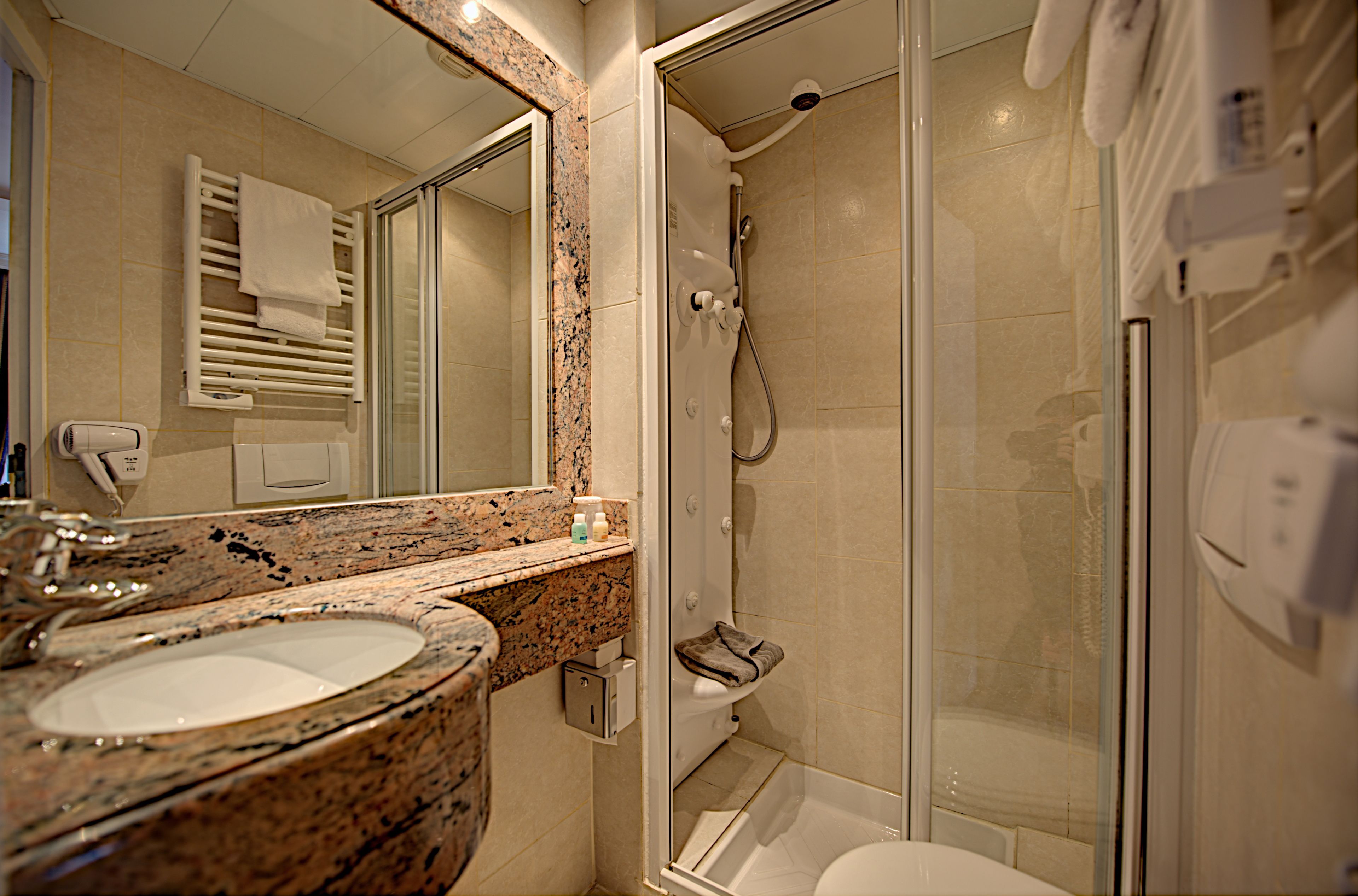 A bathroom with a granite sink, a mirror, a towel rack, a shower, and a toilet.