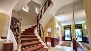 Uma escadaria com corrimão de metal, degraus carpetados e um corrimão de madeira.