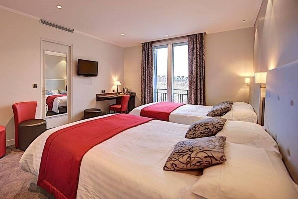 A hotel room with two beds, a desk, a chair, and a TV.