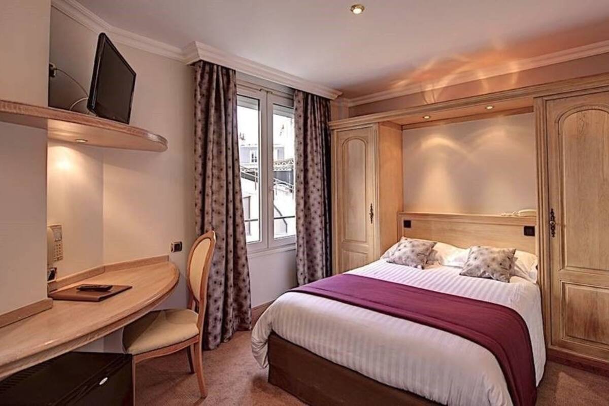 A hotel room with a bed, a desk, a chair, and a wardrobe.