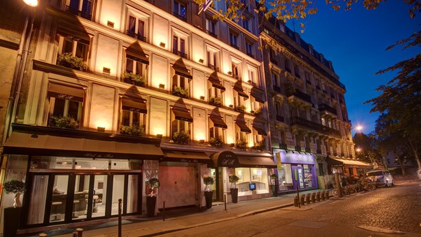 Um hotel de vários andares com estilo arquitetônico europeu clássico, com varandas com plantas, um café no nível da rua e uma fachada visível com sinalização.