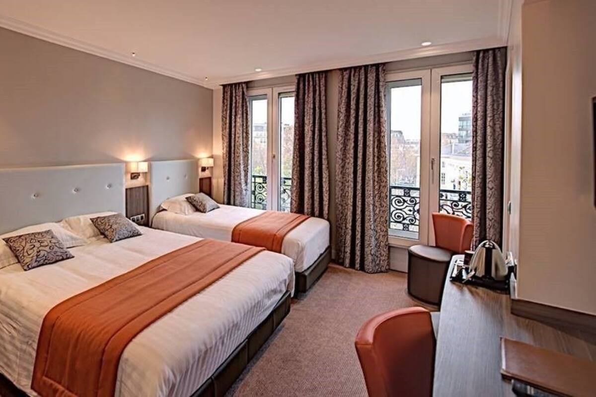 A hotel room with two beds, a desk, and a chair.