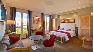 Quarto de hotel com uma cama, um sofá, uma mesa de jantar e uma cadeira. Há uma janela com cortinas, um quadro na parede e um abajur.
