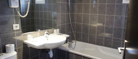 Un baño con lavamanos blanco, bañera y secador de pelo fijado en la pared.