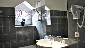 A modern bathroom with dark tiles, a sink, a mirror, a shower, and a hairdryer on the wall. - Hôtel Alliance Lourdes (Lourdes)