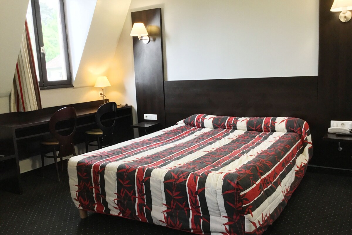 A hotel room with a bed, desk, chair, and two wall-mounted lamps.