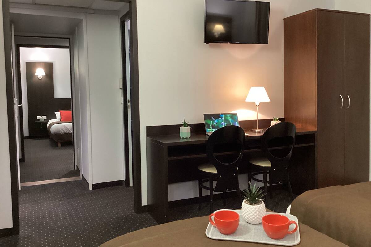 A hotel room with a bed, a desk with two chairs, a TV mounted on the wall, and a cabinet.