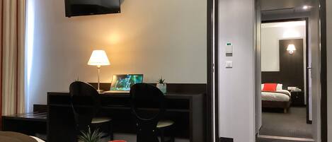 Ein Hotelzimmer mit Bett, Schreibtisch mit Laptop, Wand-Fernseher und einer Tür zu einem Badezimmer.