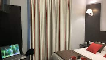 Camera d'albergo con un letto, una scrivania con un portatile, un comodino con una lampada e una finestra con tende.