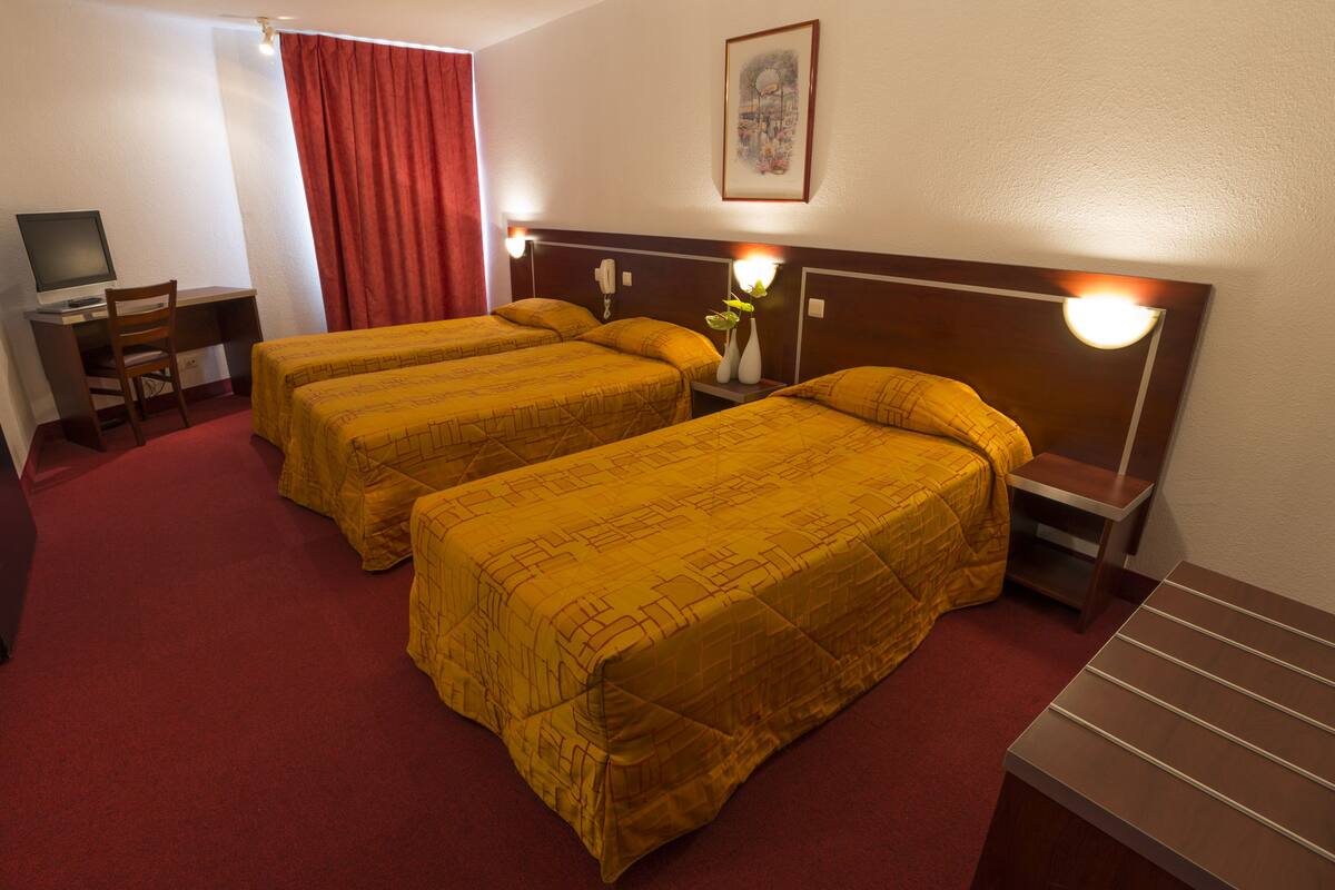 A hotel room with two beds, a desk with a computer, a chair, and a nightstand with a lamp.