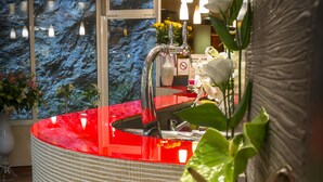 A modern bathroom with a red countertop, a sink, and a mirror. There are hanging lights and a window with a view of trees. - America Hotel Lourdes (Lourdes)
