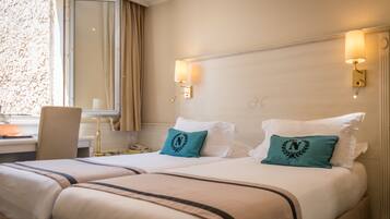 A hotel room with two beds, a desk with a lamp, and a window with curtains.