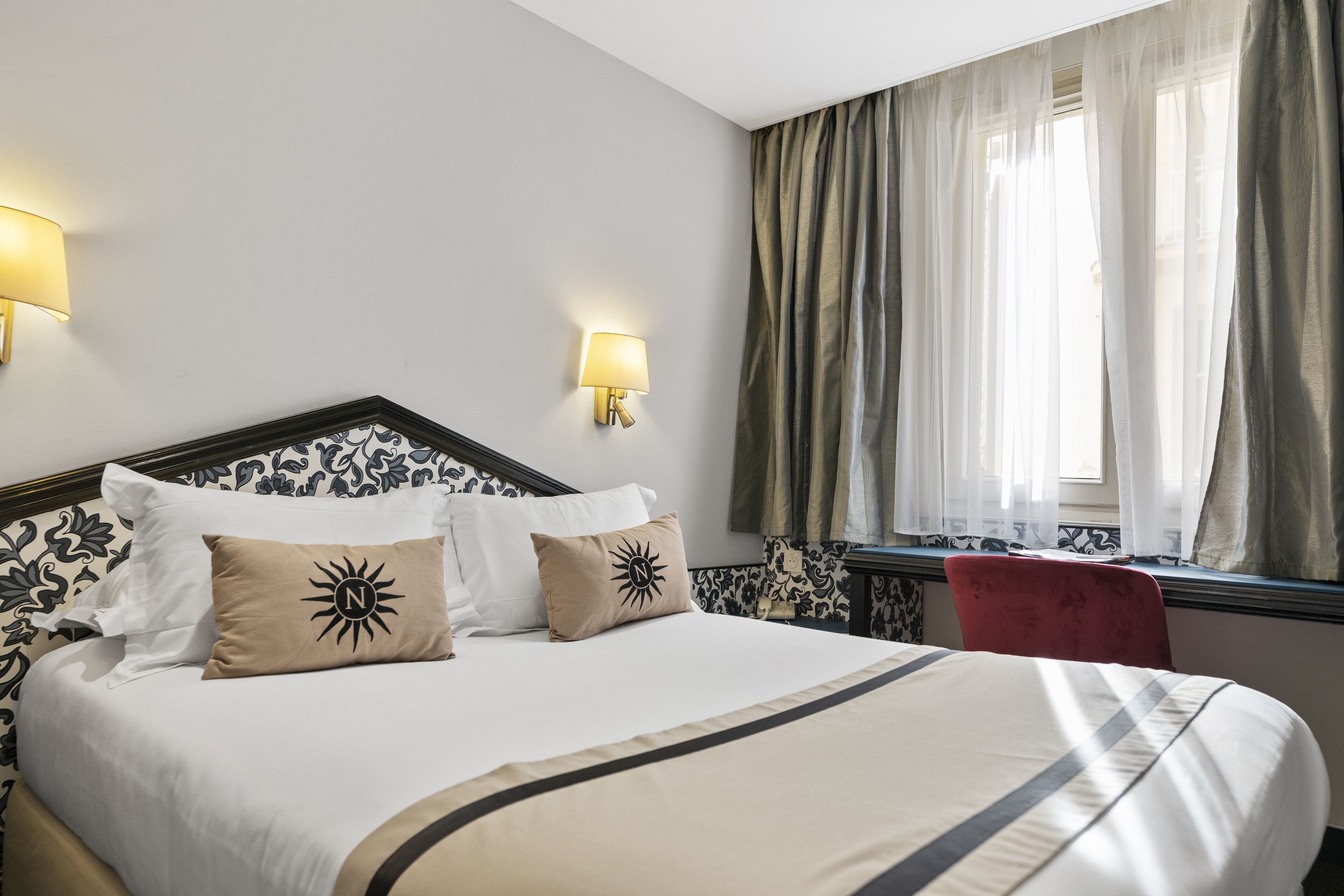 Una cama bien hecha con cabecera, dos lámparas de pared y una ventana con cortinas.