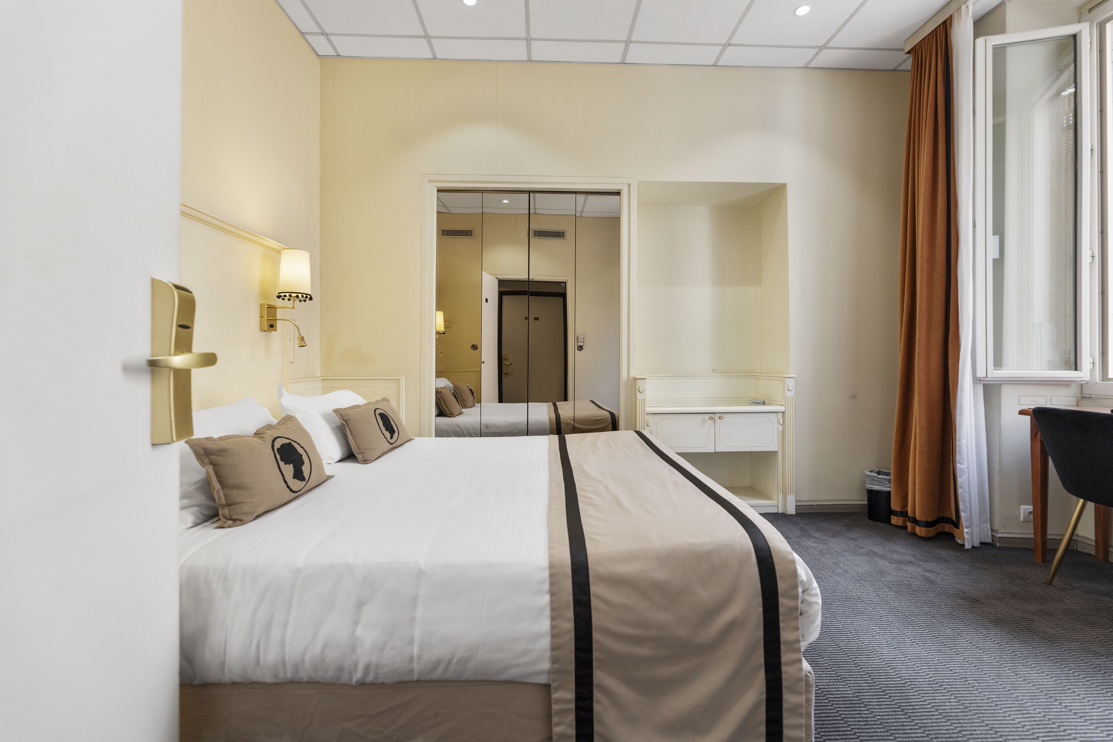 Hotellihuone, jossa on suuri sänky, työpöytä, tuoli ja peili.
