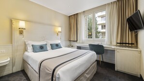 A hotel room with a bed, bedside table, desk, chair, TV, and window with curtains.