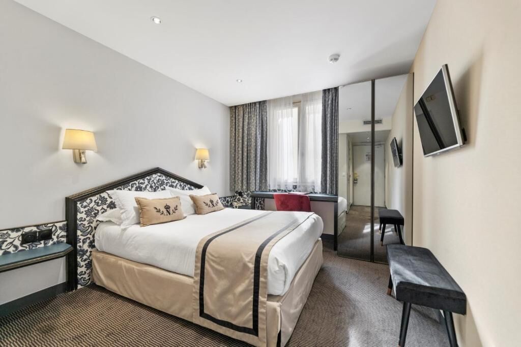 A hotel room with a bed, bedside tables, a desk, a chair, a TV, and a mirror.