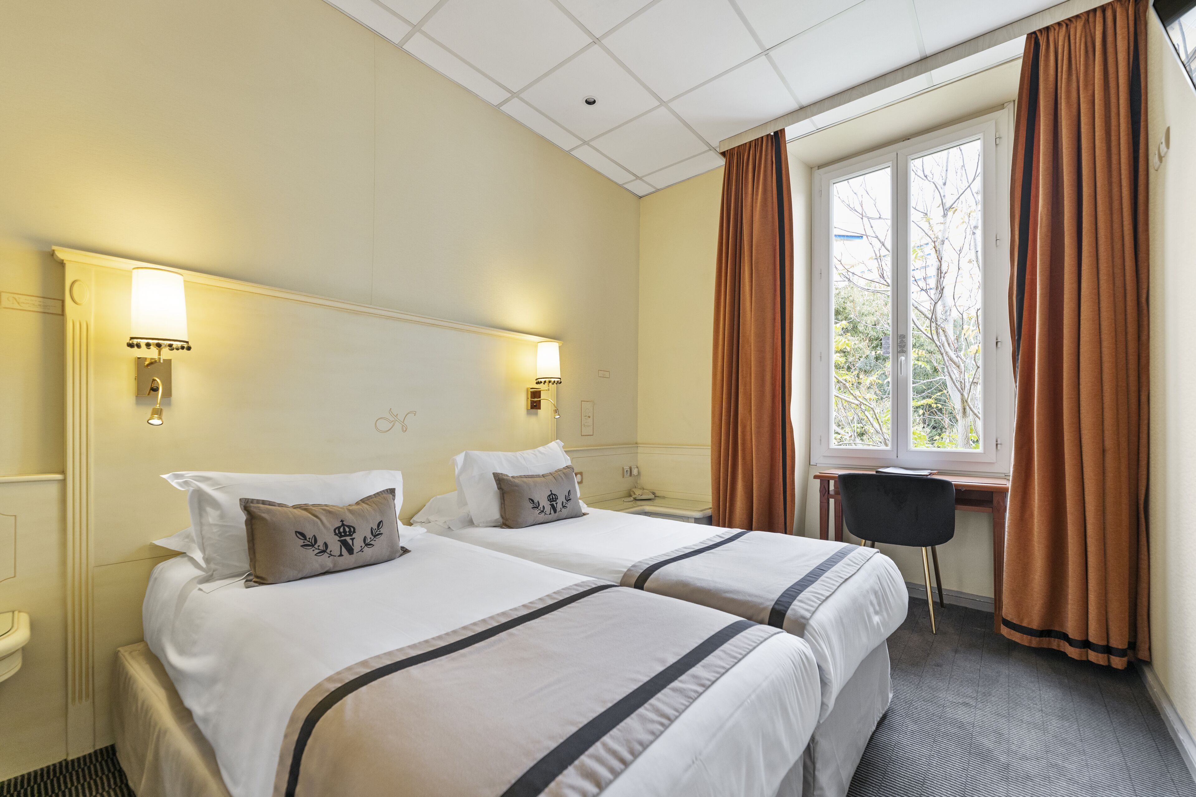 Une chambre d’hôtel avec deux lits, un bureau et une fenêtre avec des rideaux.
