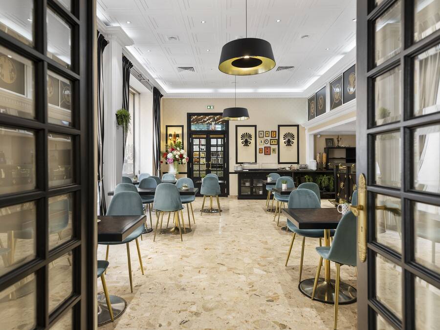Uma ampla área de jantar com piso de mármore, cadeiras modernas e uma luminária pendente preta central.