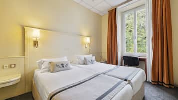 Een hotelkamer met twee bedden, een nachtkastje, een bureau en een raam met gordijnen.