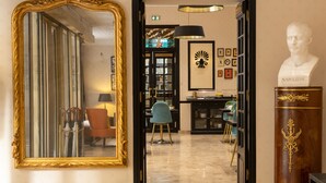 A grand hallway with a large ornate mirror, a bust of Napoleon, a wooden bust with a decorative base, and a library filled with books and framed pictures.