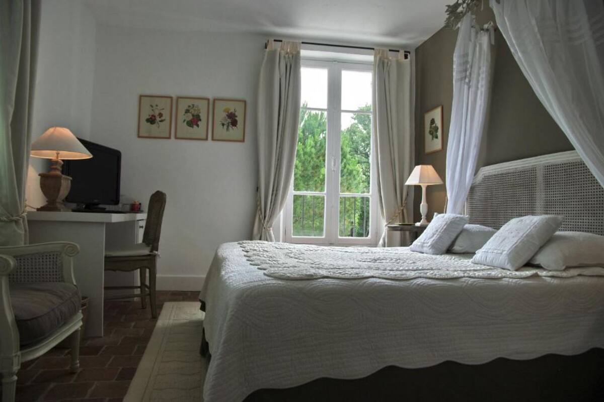 A bedroom with a large bed, a desk, a chair, and a window with curtains.