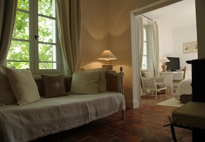A cozy bedroom with a bed, a bedside table with a lamp, a chair, and a view of the outdoors through a window. - Le Mas de Chastelas (Gassin)