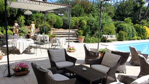 Un patio al aire libre con mobiliario de mimbre, una piscina y un jardín con estatuas.
