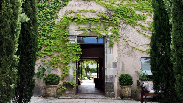 Un edificio con fachada de piedra, contraventanas verdes y un porche cubierto.