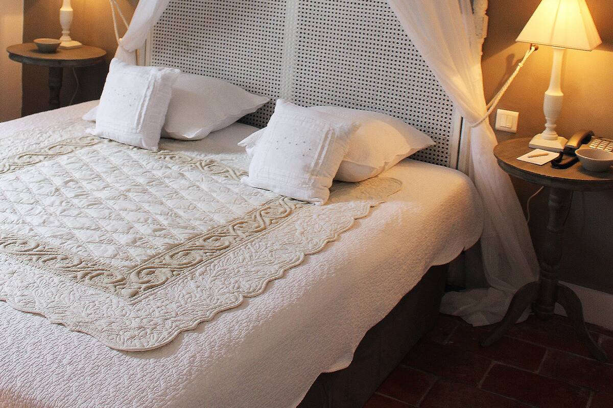 A neatly made bed with a canopy, two bedside lamps, and a small table with a phone and a bowl.