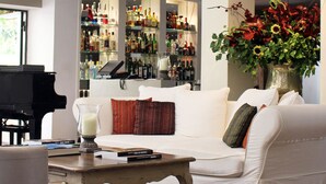 Una sala moderna con un sofá blanco, una mesa de centro de madera y un piano de cola negro. Hay una zona de bar con estantes llenos de botellas y un gran jarrón de flores.