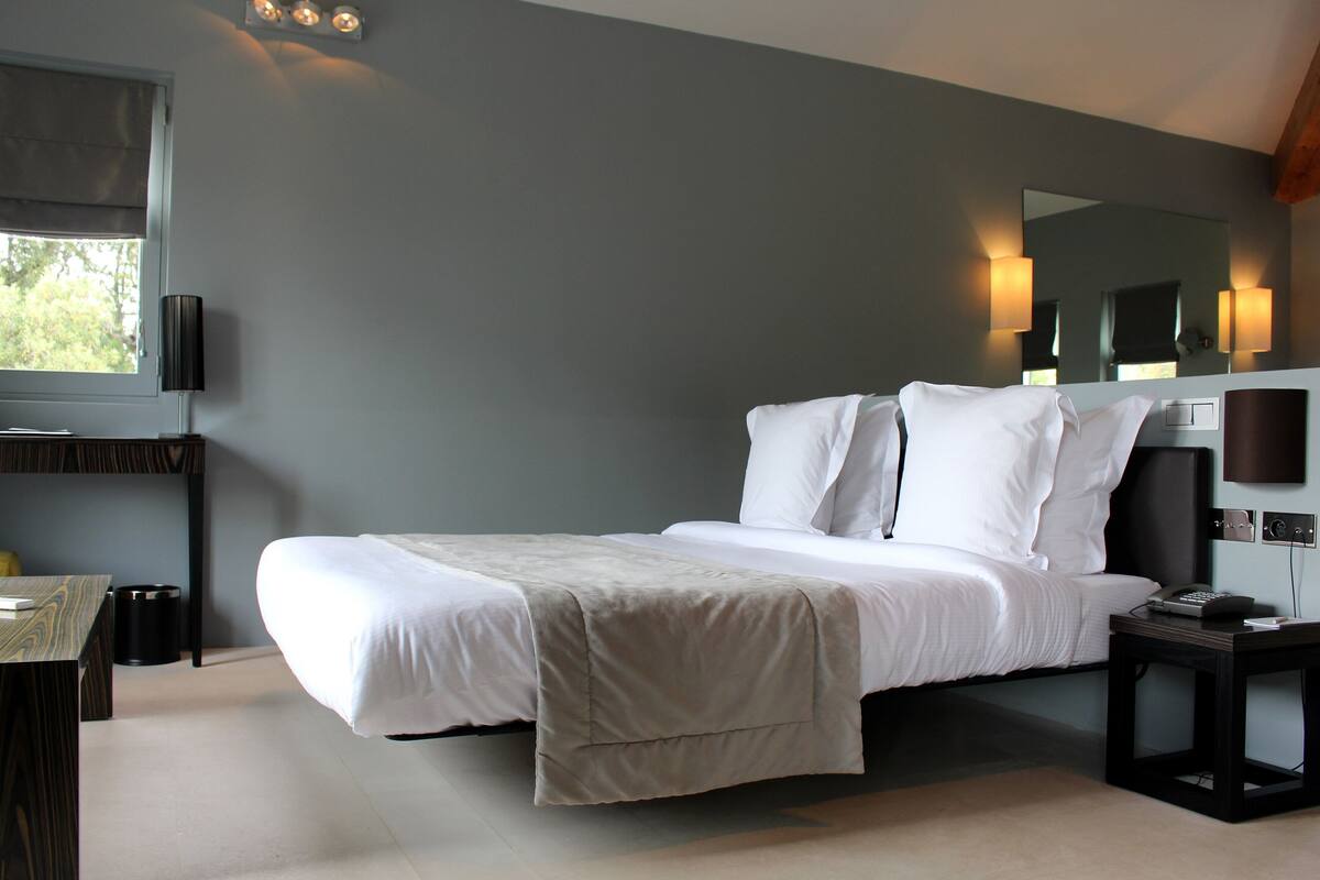 A modern hotel room with a large bed, bedside tables, a desk, and a window with a view.