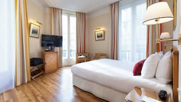 Una habitación de hotel con una cama grande, televisión, escritorio con silla y ventana con cortinas.
