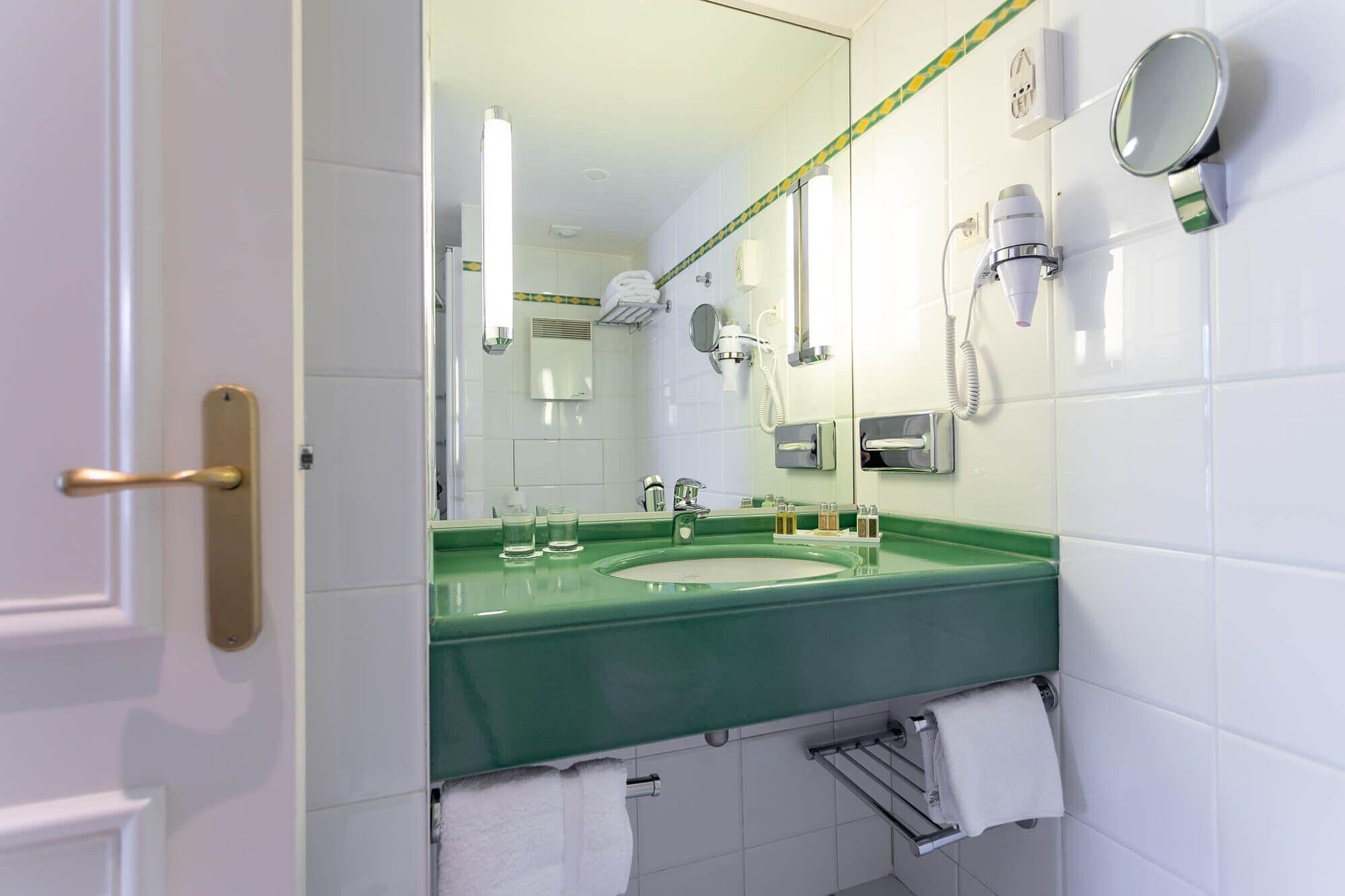 A bathroom with a green sink, white tiles, a towel rack, a mirror, and a hairdryer.