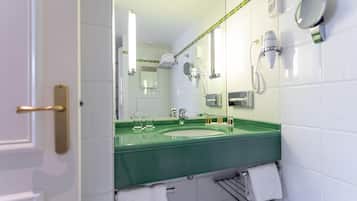 A bathroom with a green sink, white tiles, a towel rack, a mirror, and a hairdryer.