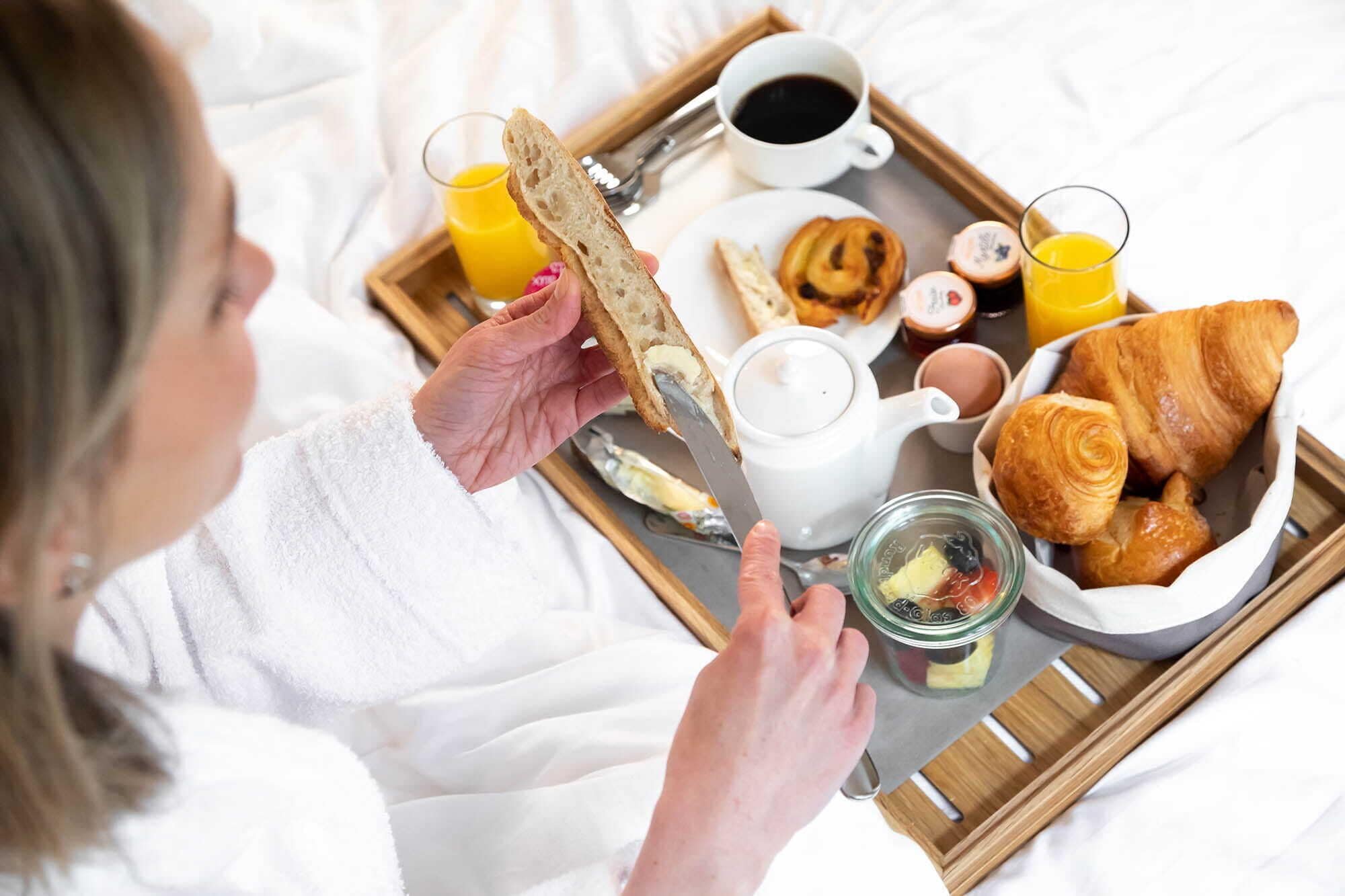 A breakfast tray with croissants, a croissant sandwich, a glass of orange juice, a cup of coffee, and a small bowl of jam.