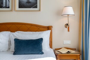 A neatly made bed with white and blue pillows, a wooden headboard, a bedside table with a book, and a wall-mounted lamp.