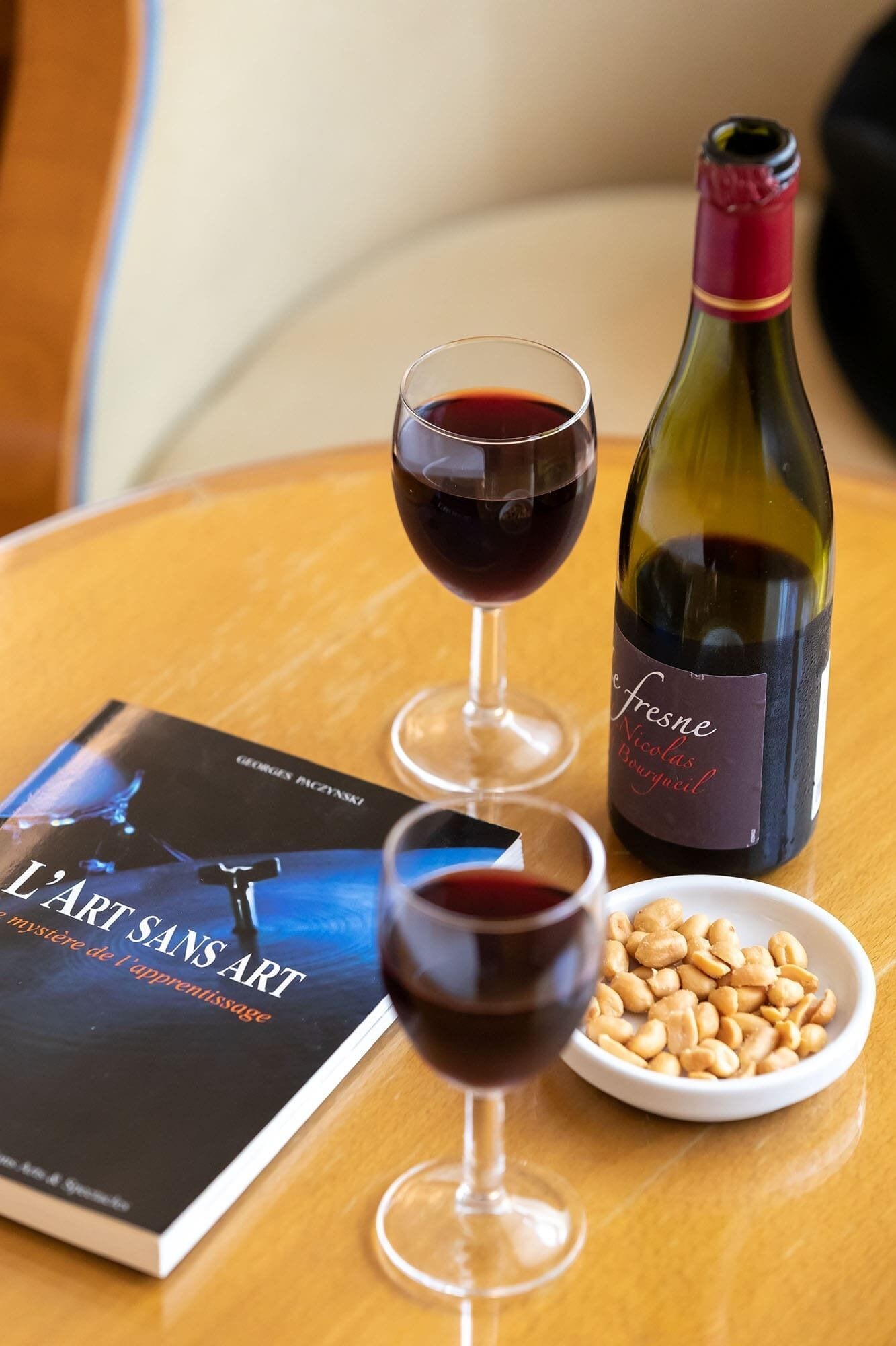 Una mesa con dos copas de vino, una botella, un libro y un tazón de nueces.