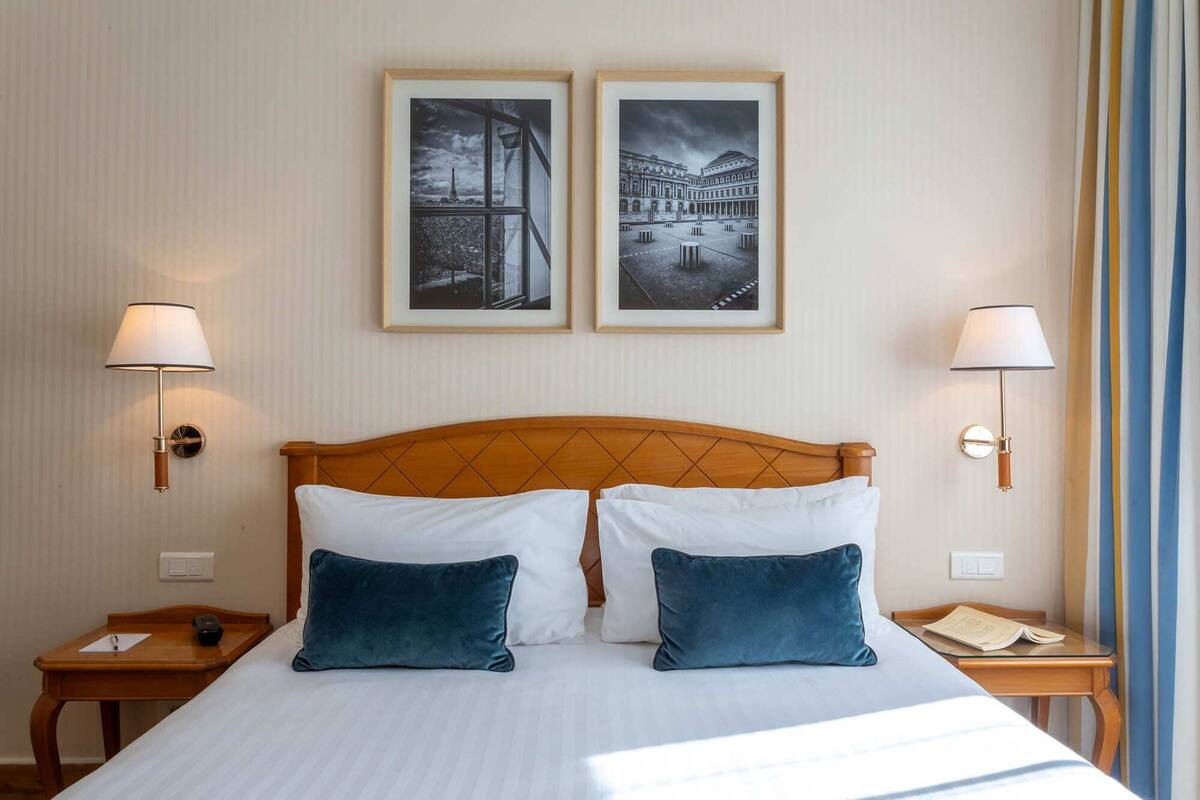 A hotel room with a bed, two bedside tables, two wall-mounted lamps, and two framed pictures on the wall.