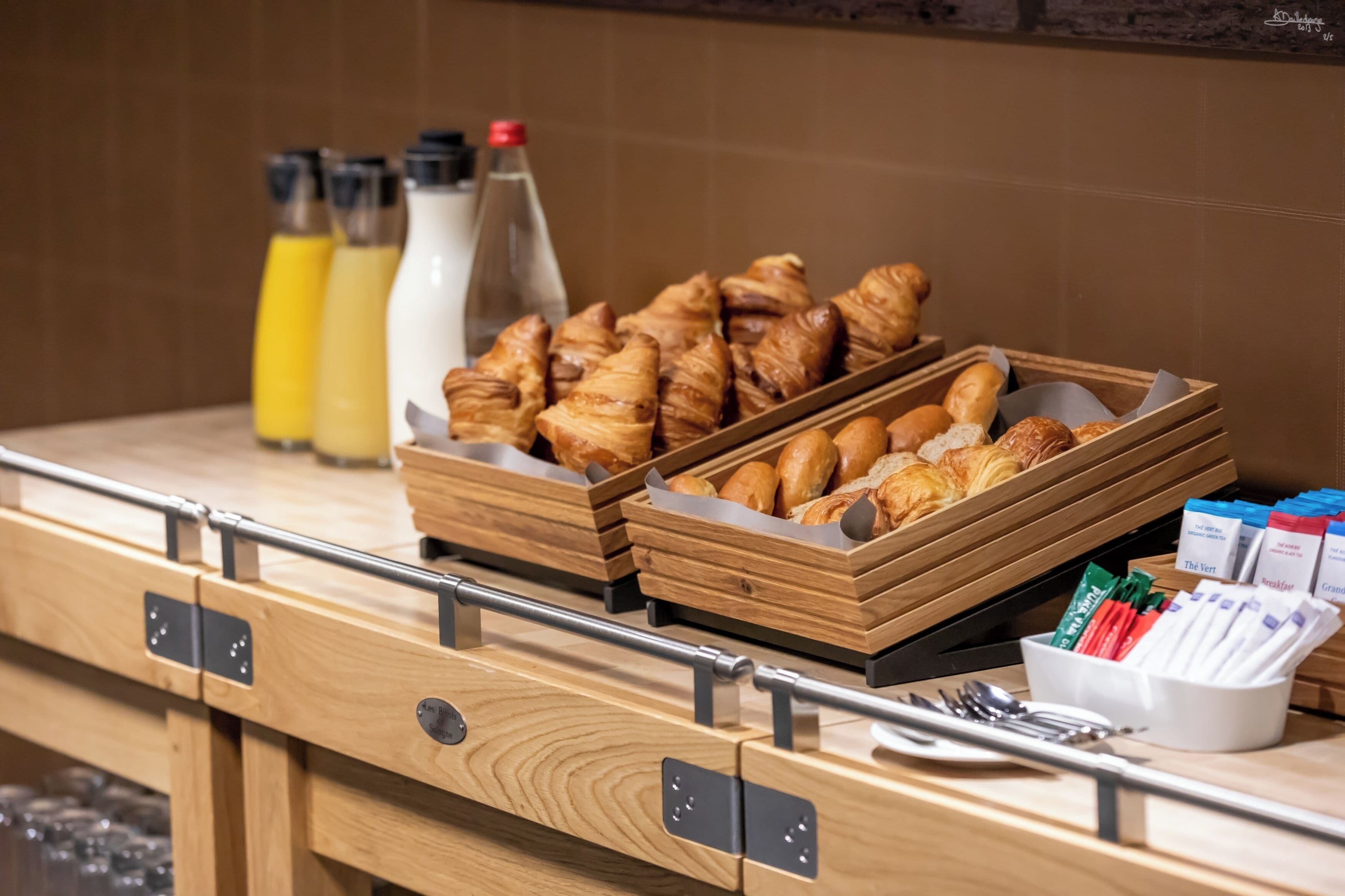 Un buffet de petit-déjeuner avec des plateaux en bois remplis de viennoiseries, des bouteilles de jus et divers aliments pour le petit-déjeuner.