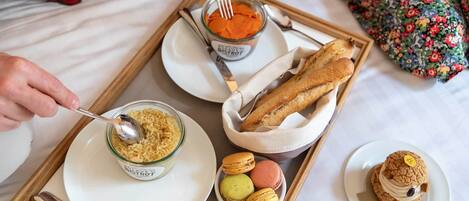 Una bandeja con un tazón de arroz, un tarro de sopa, una baguette, macarons y un postre sobre una base.