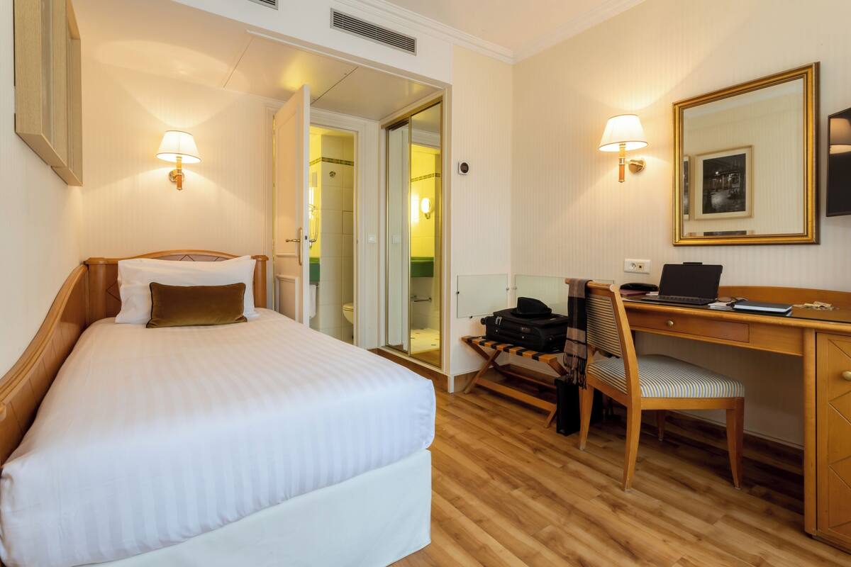 A hotel room with a bed, a desk, a chair, and a mirror.