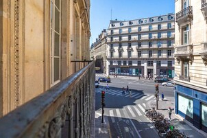 A street view with a building featuring a classic architectural style, a crosswalk, and parked bicycles.