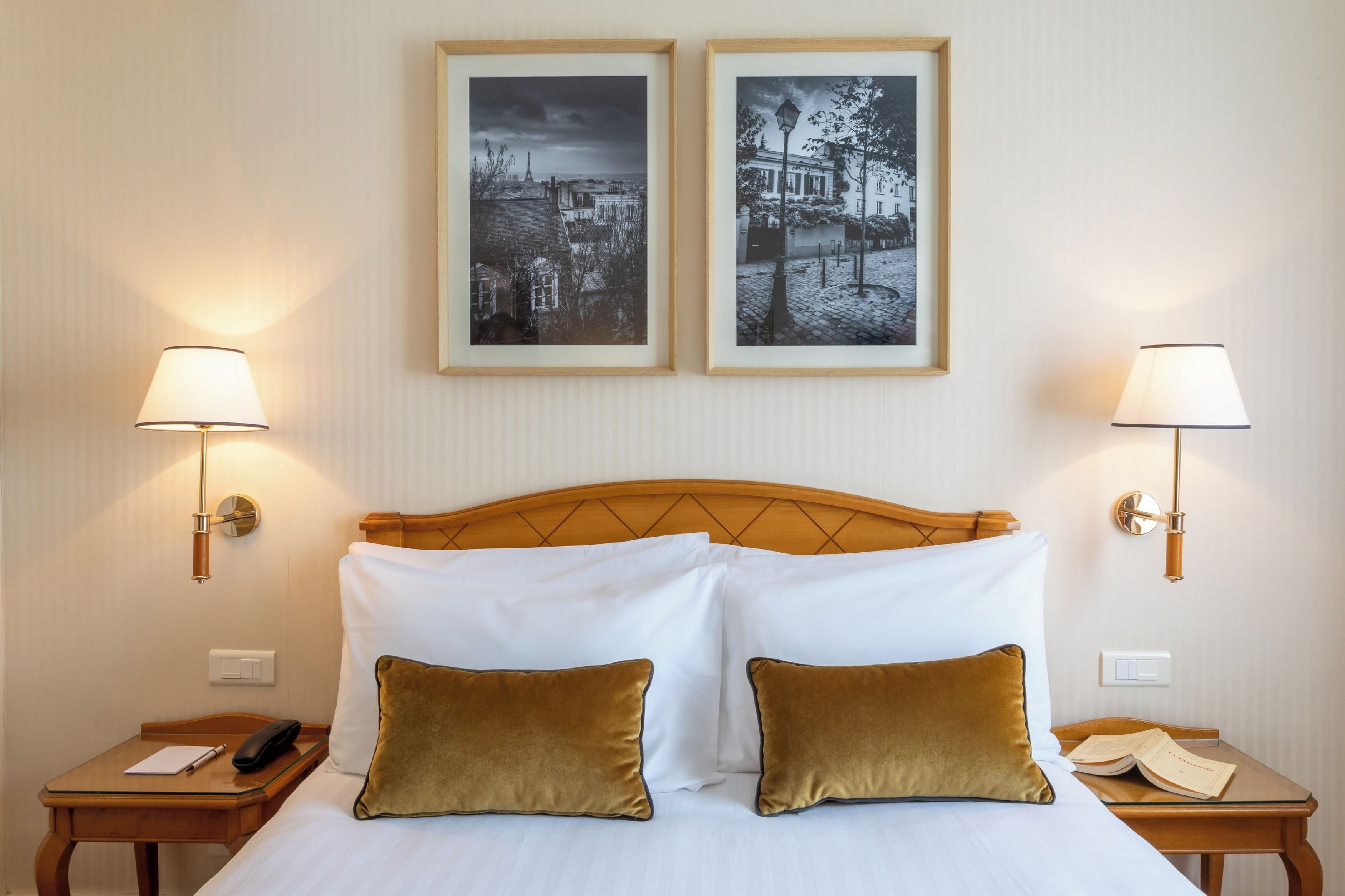 Una camera d'albergo con un letto, due comodini, una lampada per lato e due quadri appesi al muro.