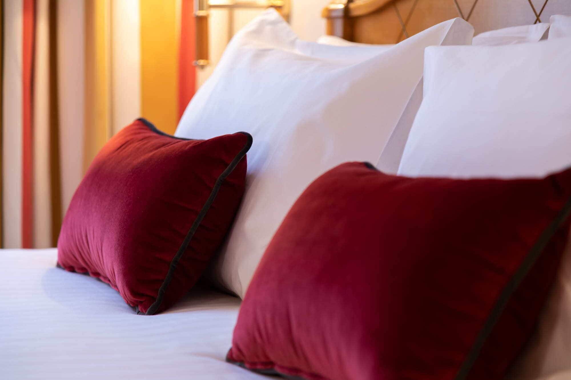 Una cama con almohadillas blancas y rojas, un cabecero de madera y una pared a rayas al fondo.
