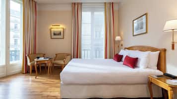 Een hotelkamer met een groot bed, een kleine tafel, twee stoelen, een nachtkastje en een raam met gordijnen.