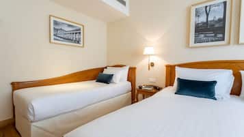 Two single beds with wooden headboards, white bedding, and a nightstand with a lamp and a book.