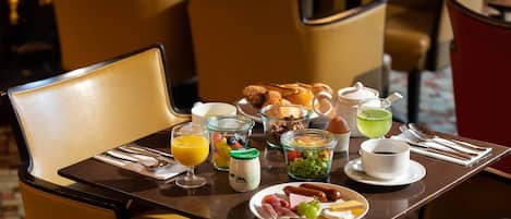 A breakfast setting with a variety of food items, including eggs, sausages, and fruits, on a table with a teapot and cups.