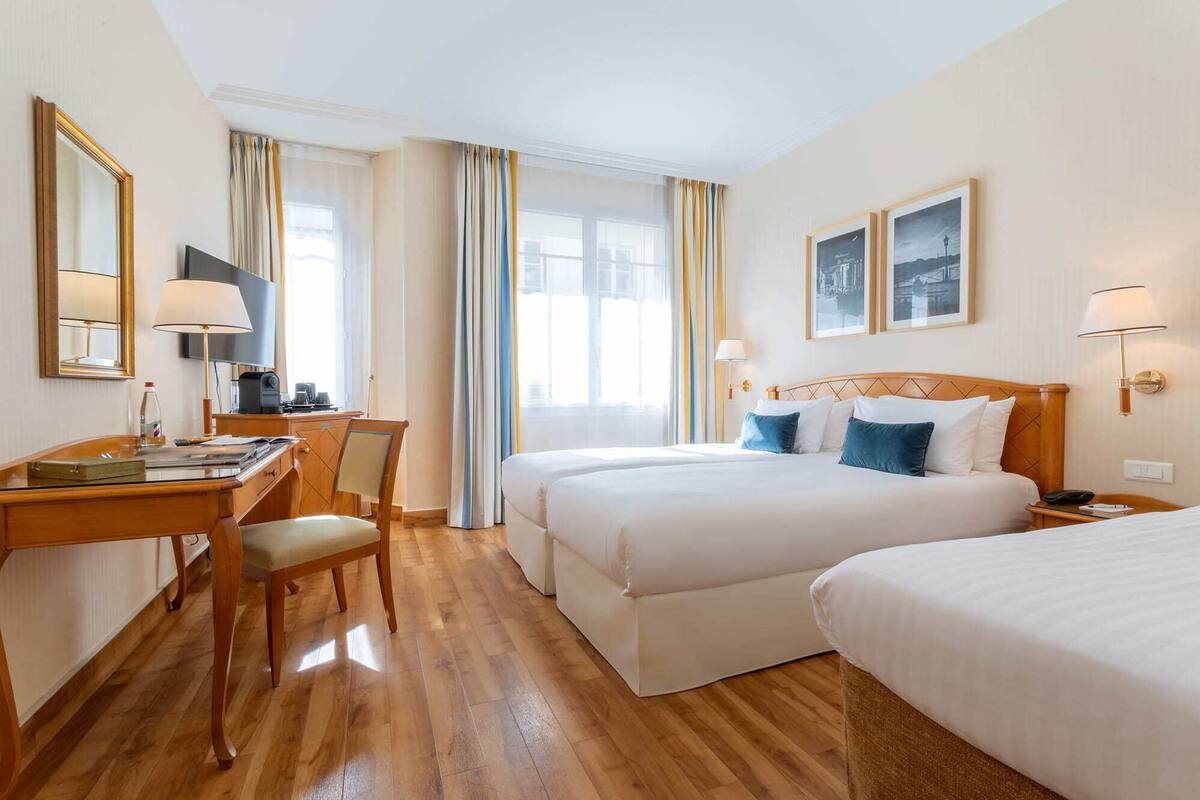 A hotel room with two beds, a desk with a chair, a television, and a window with curtains.