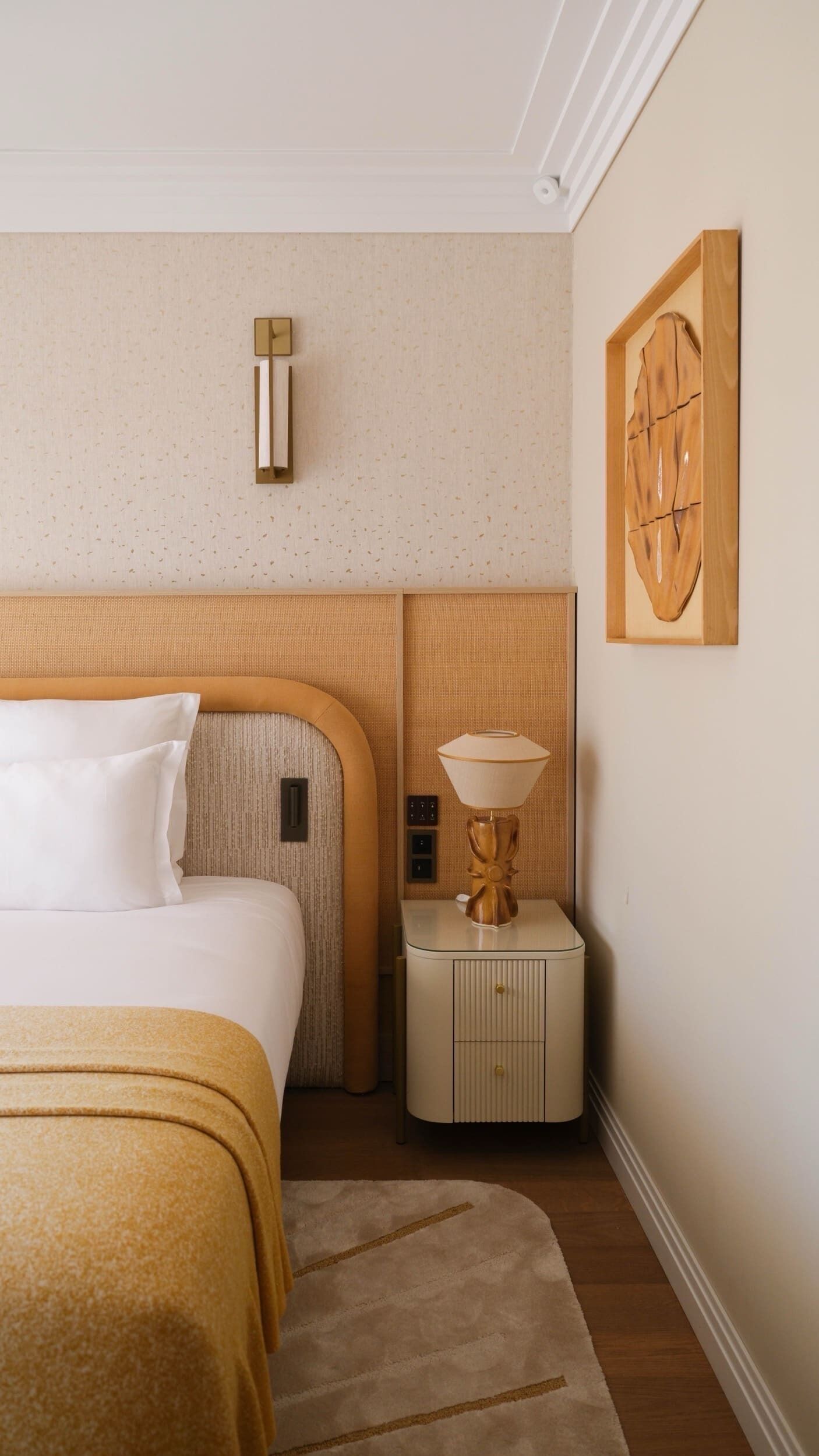 A hotel room with a bed, bedside table, lamp, wall clock, and artwork.