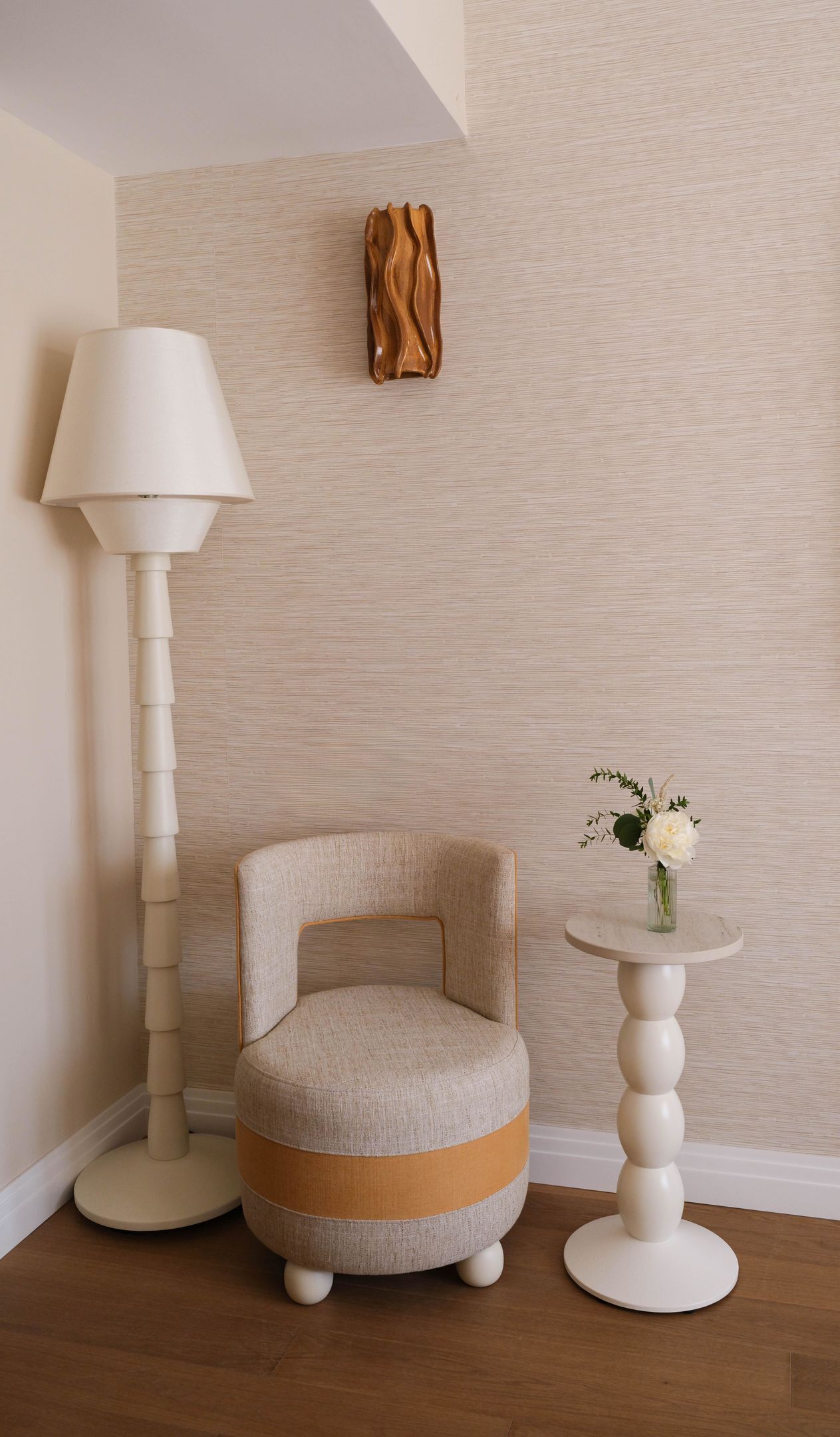 Une pièce avec un fauteuil rond, un lampadaire et une petite table sur laquelle est posé un vase de fleurs.